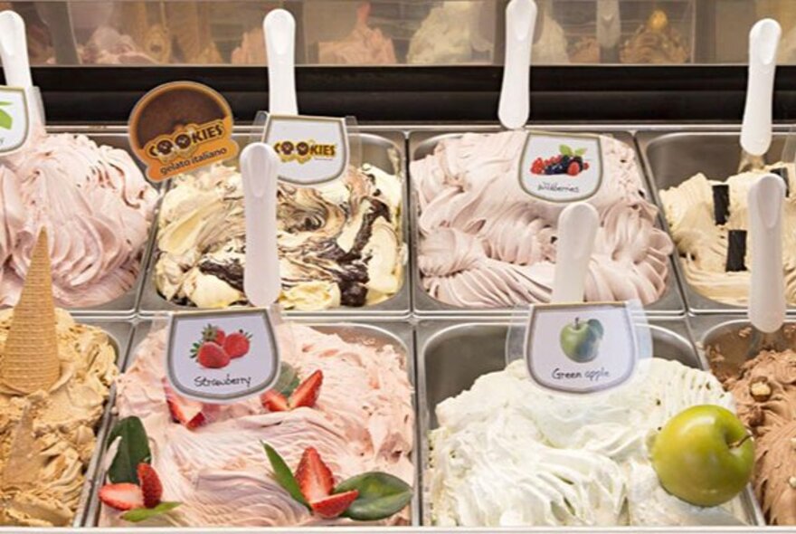 A selection of gelato in stainless steel tubs underneath a glass display.