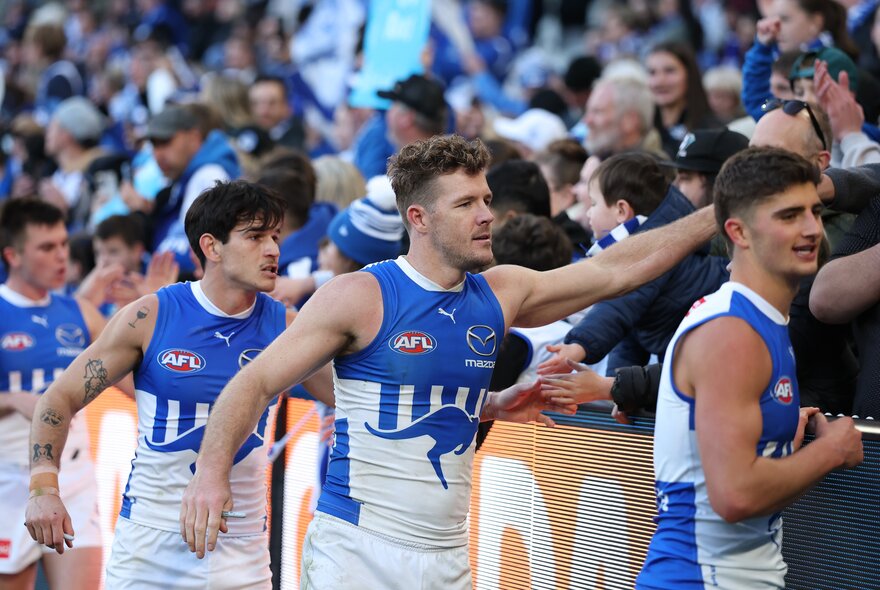 North Melbourne AFL football players leaving the football field and greeting their fans with high-fives as they walk past the boundary fence.