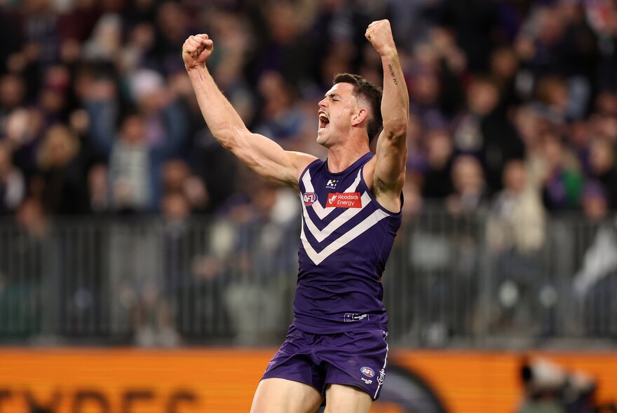 A Fremantle AFL player with his arm raised above him on the football field during a match.