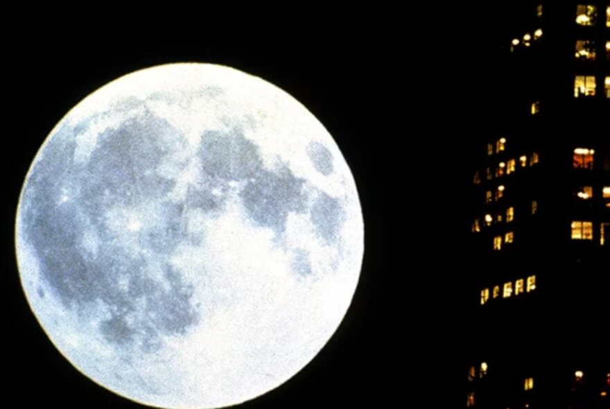 A huge full moon seen next to an inner city office building at night.