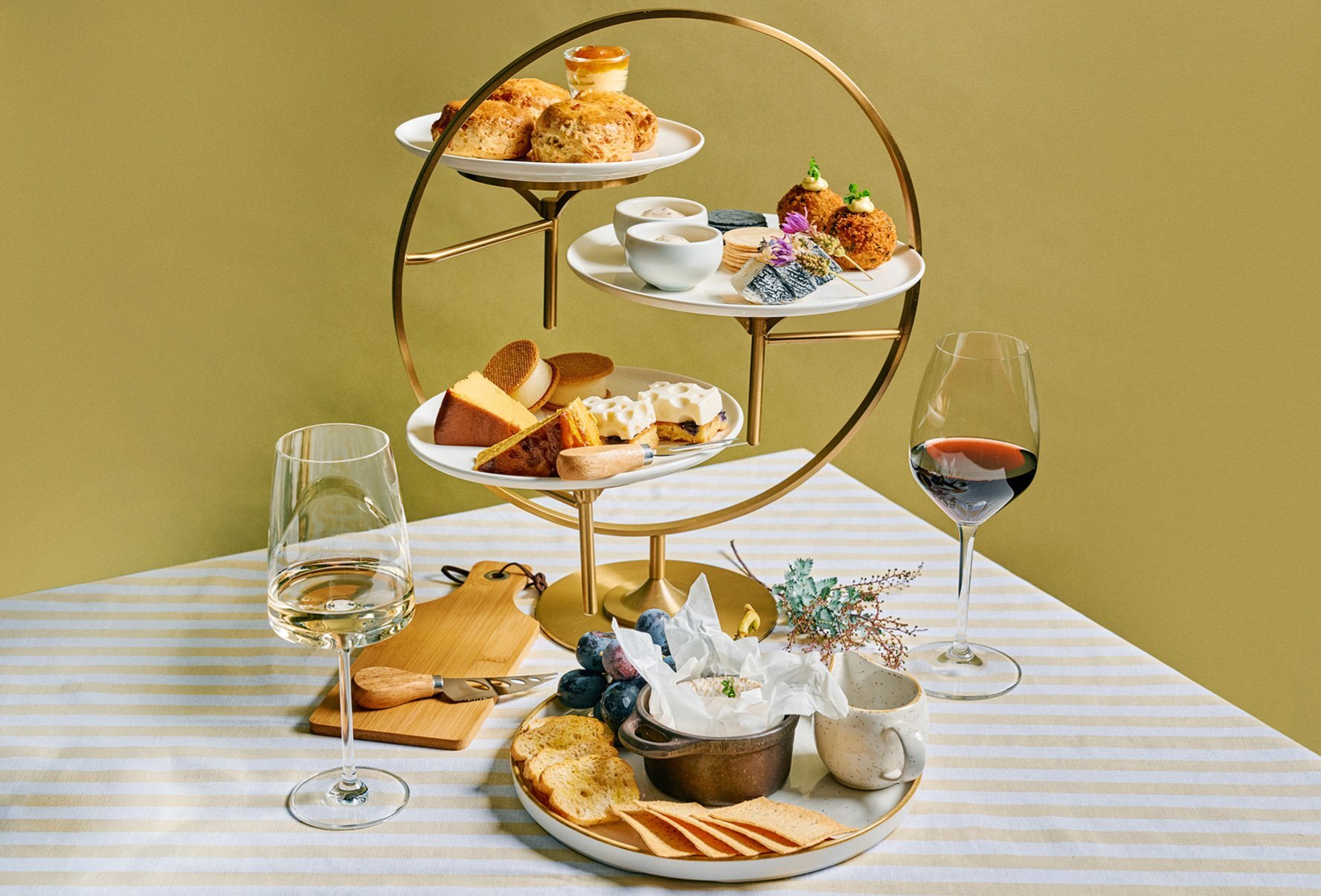 A gold high tea tray with wine and cheese.