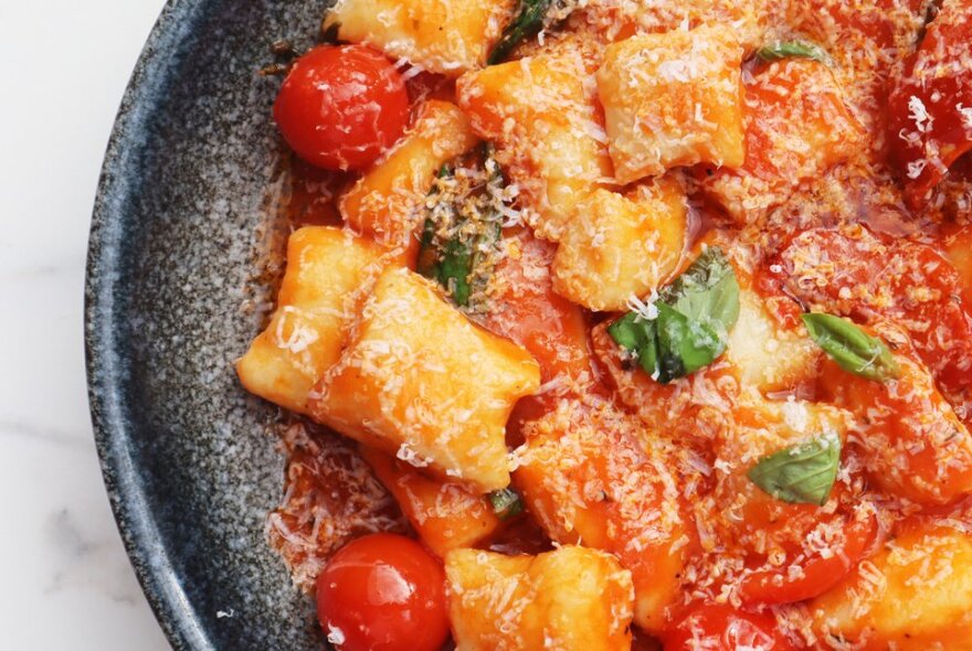 A close-up of a bowl of gnocchi with cherry tomato sauce, parmesan and basil leaves. 