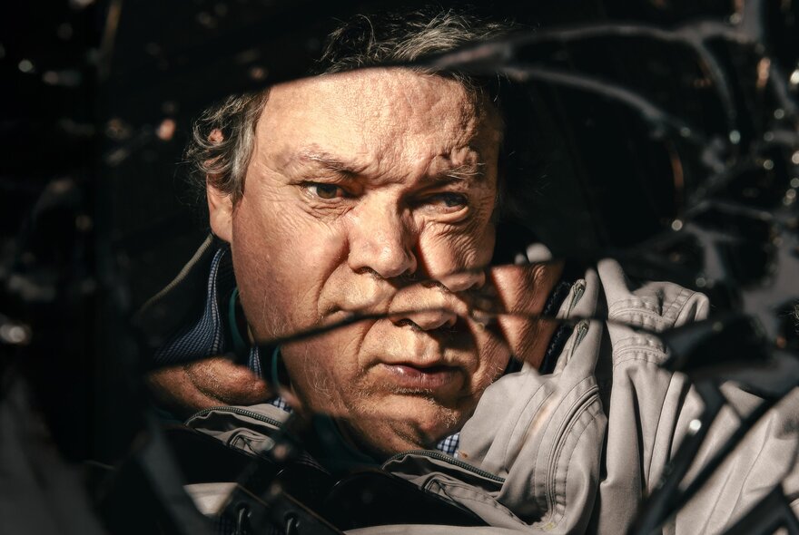 An image of a man's face with a neutral expression, fractured like a cracked mirror.