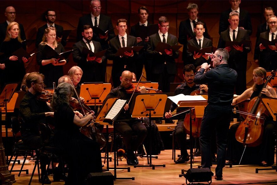 A symphony orchestra and vocal choir performing on a stage, with a conductor leading them.
