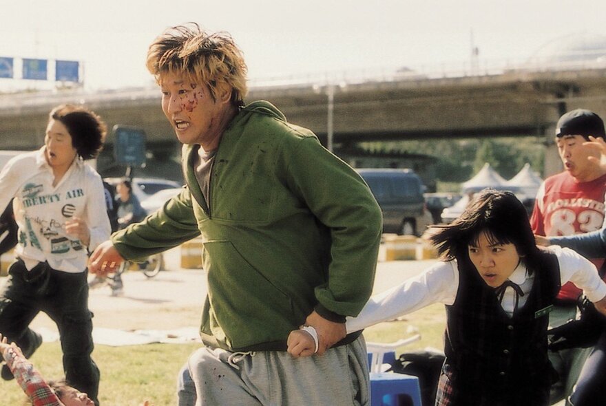 A still from a Korean horror film showing four people running away from something, a man in the front covered in blood.