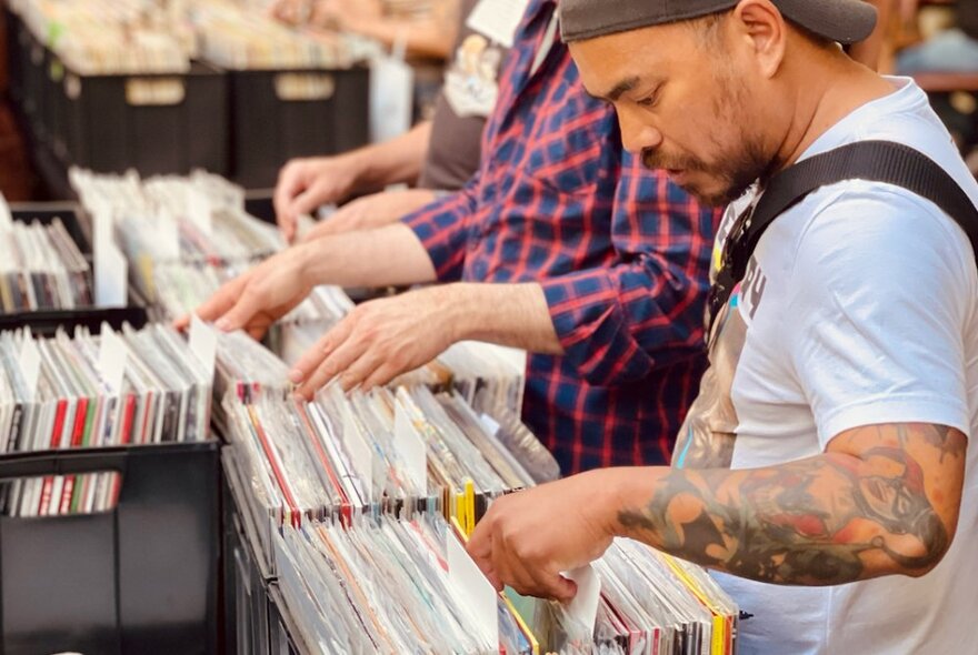 Several people in profile flicking through crates of vinyl records at a record fair market stall.