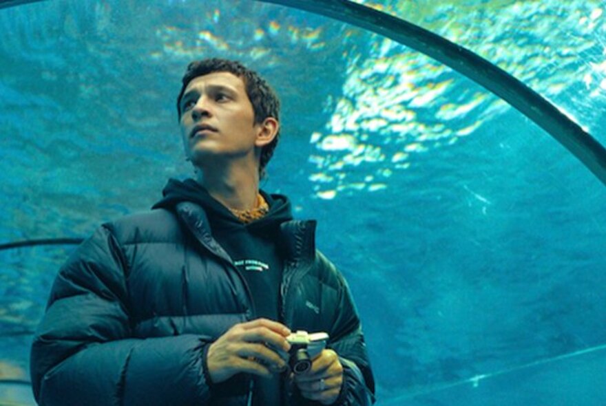 Man standing in an underwater aquarium tunnel with blue water overhead.