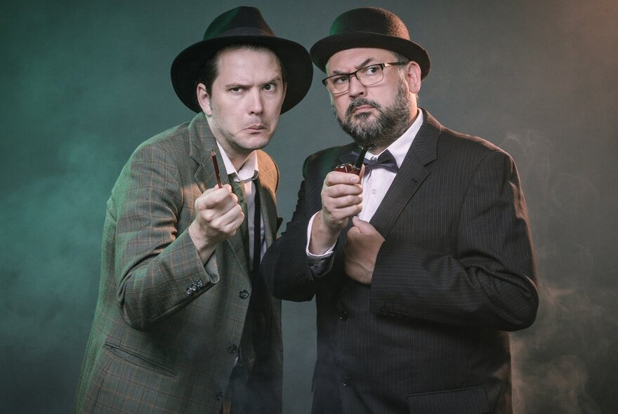 Two actors of the impro cast of a play, based on an Agatha Christie-style whodunnit, both wearing 1950s-style suits and hats.