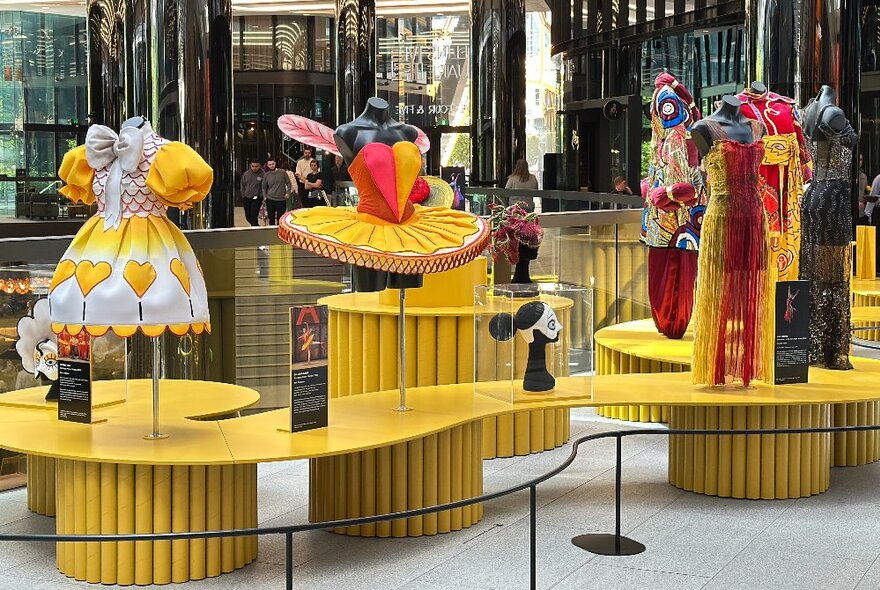 A fashion display in an open area with costumes on yellow stands. 