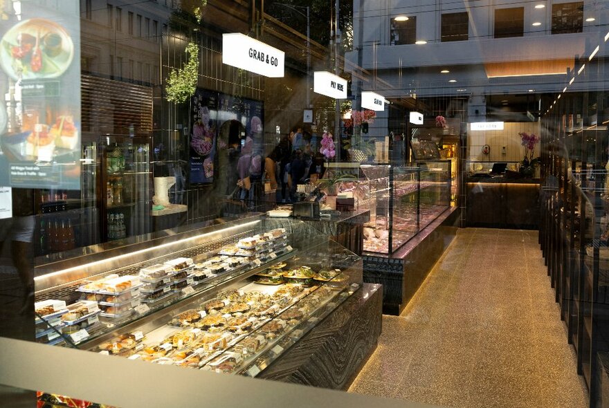 Looking at the interior of an up-market butchery and shop with goods behind glass cases. 