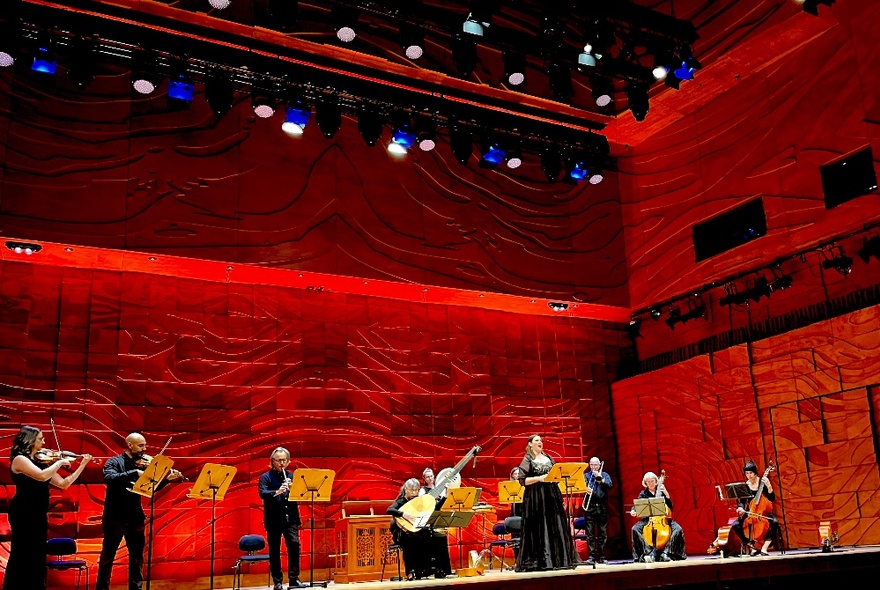 Classical musicians performing on stage under red lighting.