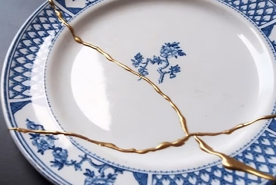 A broken blue and white china plate mended using gold highly visible glue.