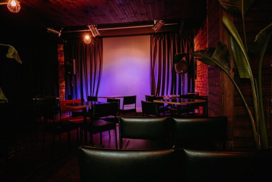 The purple-lit stage at the Motley Bauhaus, seen from behind empty audience chairs.