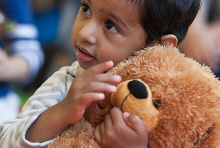 Child holding a large brown teddy, stroking its nose.