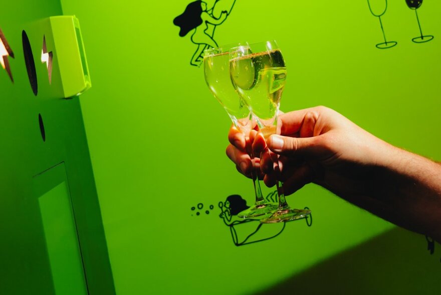 Hands clinking glasses of bubbles against a green background.