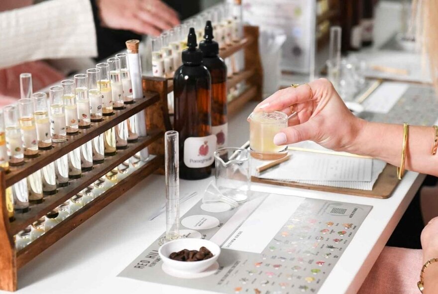 A hand selecting and mixing ingredients at a workstation in front of oils and fragrances during a perfume-making workshop.