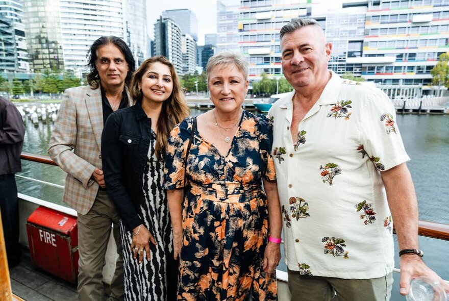 A group of four people posing for a photo on board the Lady Cutler Melbourne Showboat, with the harbour and city buildings in the background.