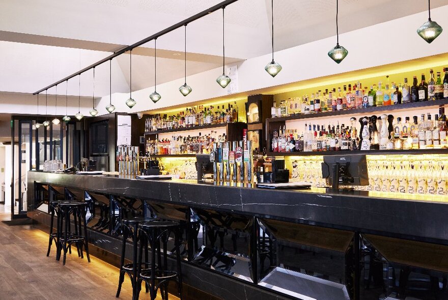 Hotel main bar with black counter and illuminated bottles lined up in the background.