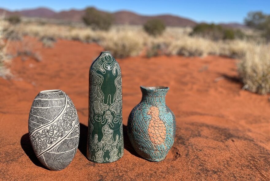 Three decorated pottery vessels on red soil in the Australian outback. 