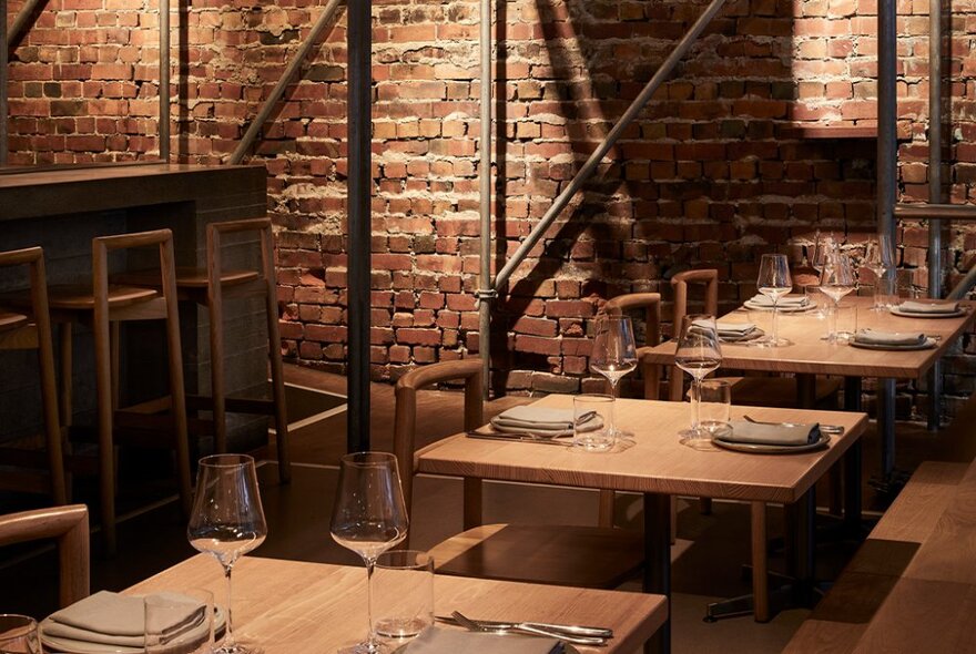 Pale wooden tables set with crockery, cutlery, napkins and glasses inside the brick walled softly lit interior of Sunda restaurant.