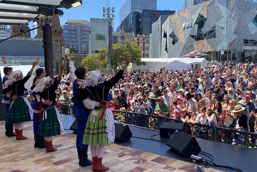 Polish dancers on stage waving at a crowd at Melbourne's Federation Square.