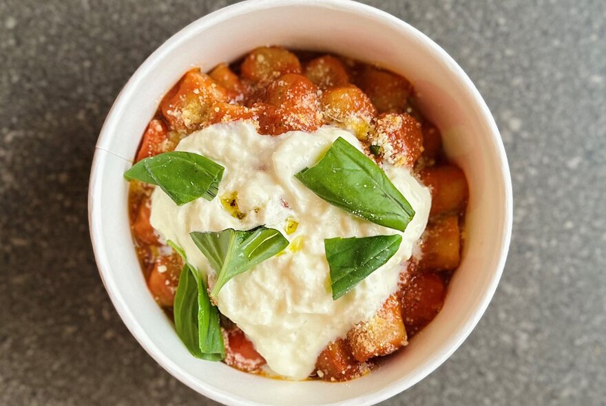 A bowl of gnocchi with a tomato based sauce, cheese and basil on top.