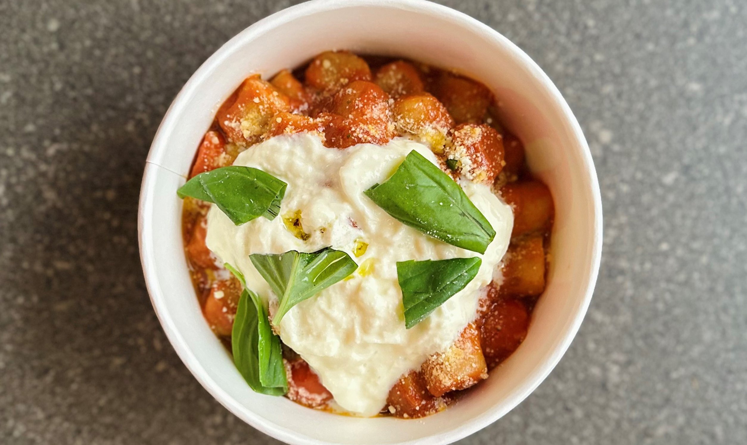 A bowl of gnocchi with a tomato based sauce, cheese and basil on top. 