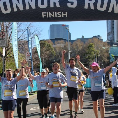 A group of people running across the finish line with a banner above them reading CONNOR'S RUN FINISH.