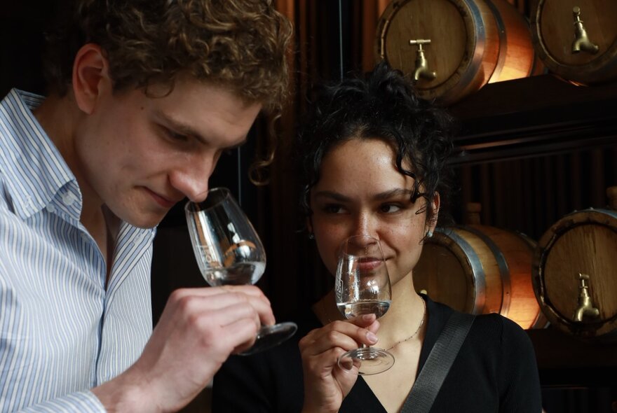 Two people smelling wine from glasses in a cellar setting as part of a wine tasting experience.