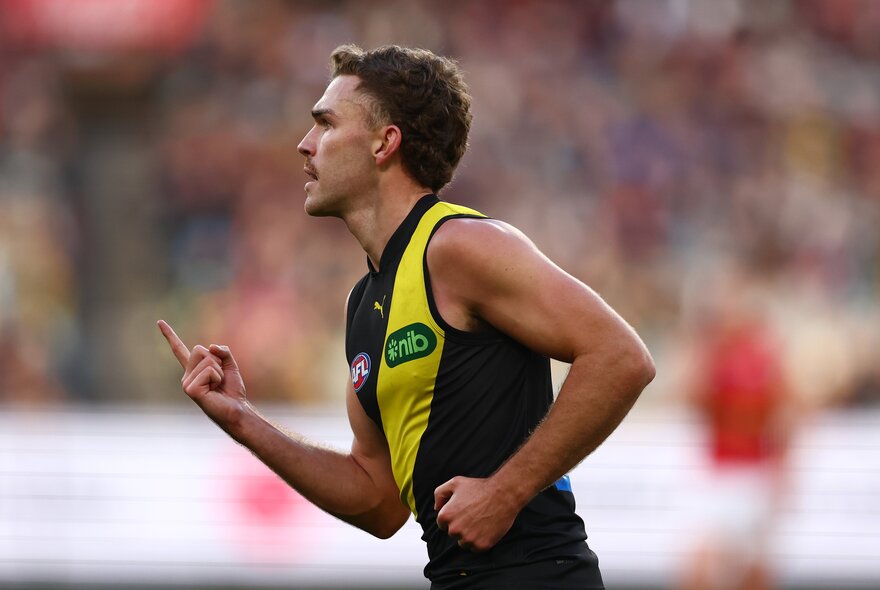 A Richmond AFL football player celebrating  with his arms pointed in front of him on the field during a match.