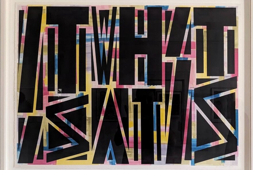 A graphic artwork featuring black block letters on a colourful background, forming the words, 'It is what it is'.