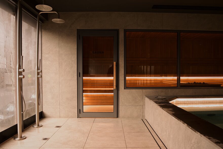 Moody, soft lighting inside a bathhouse looking towards a sauna behind glass windows. 