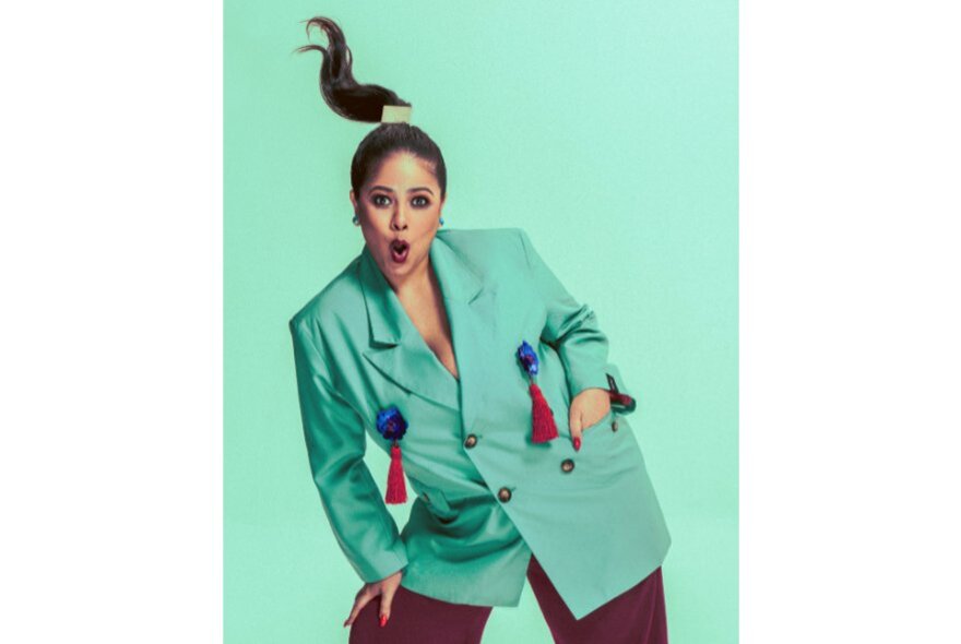 Woman with hands in her blazer pocket, hand on her knee, her pigtail flying above her head.