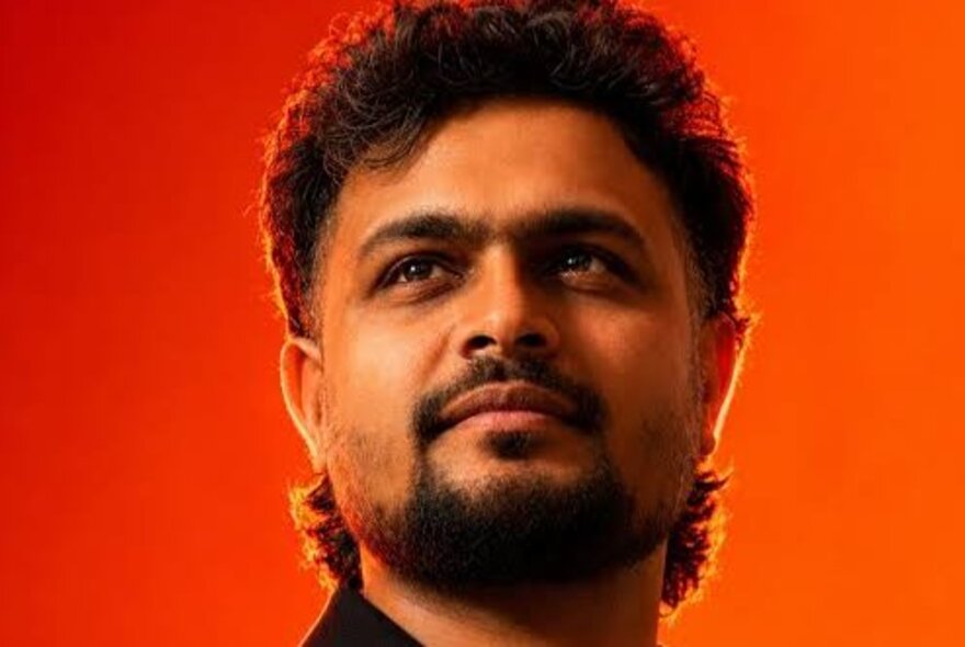 A man looking in to the distance with a satisfied look on his face against a bright orange background. 