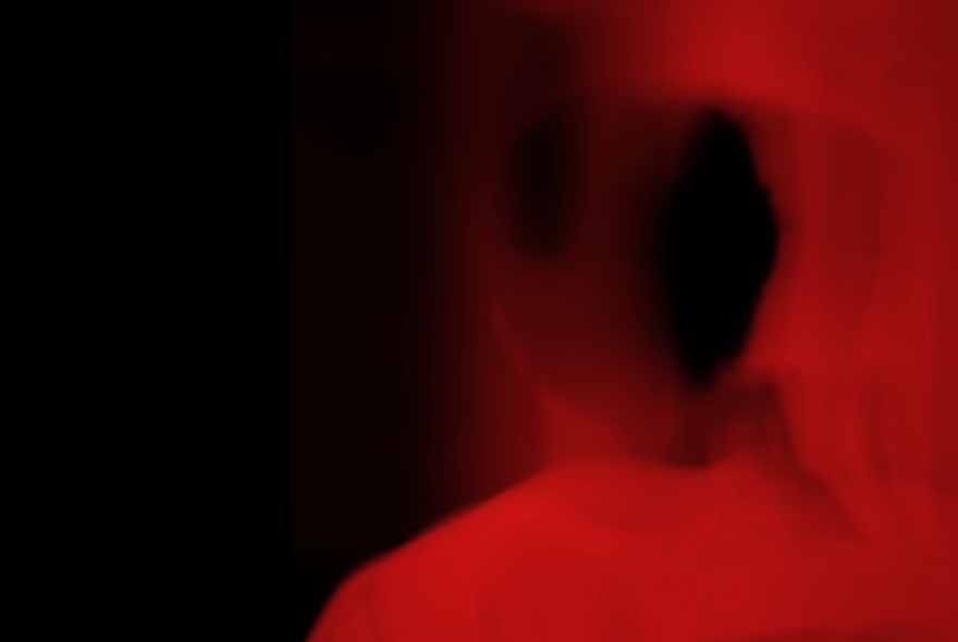 A very blurry red and black image with the vague outline of a person just able to be seen.