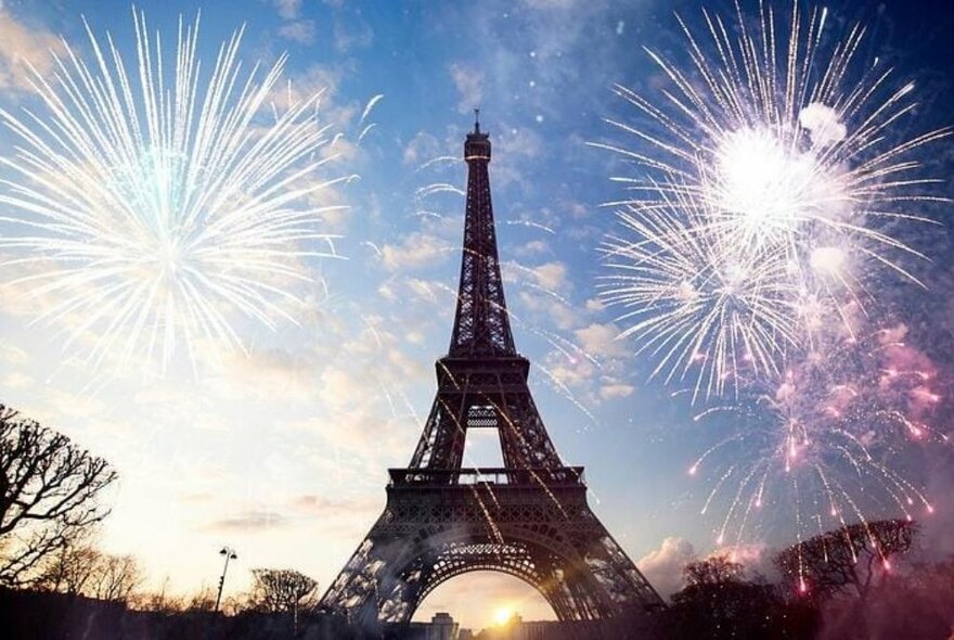 Eiffel Tower at dusk surrounded by fireworks.