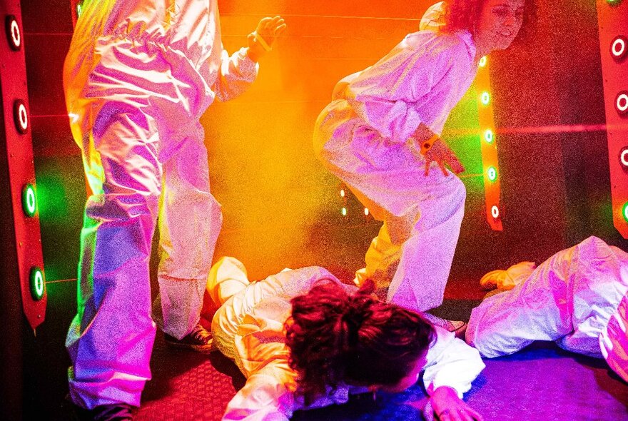 People wearing white satin suits in a brightly lit arcade games room.