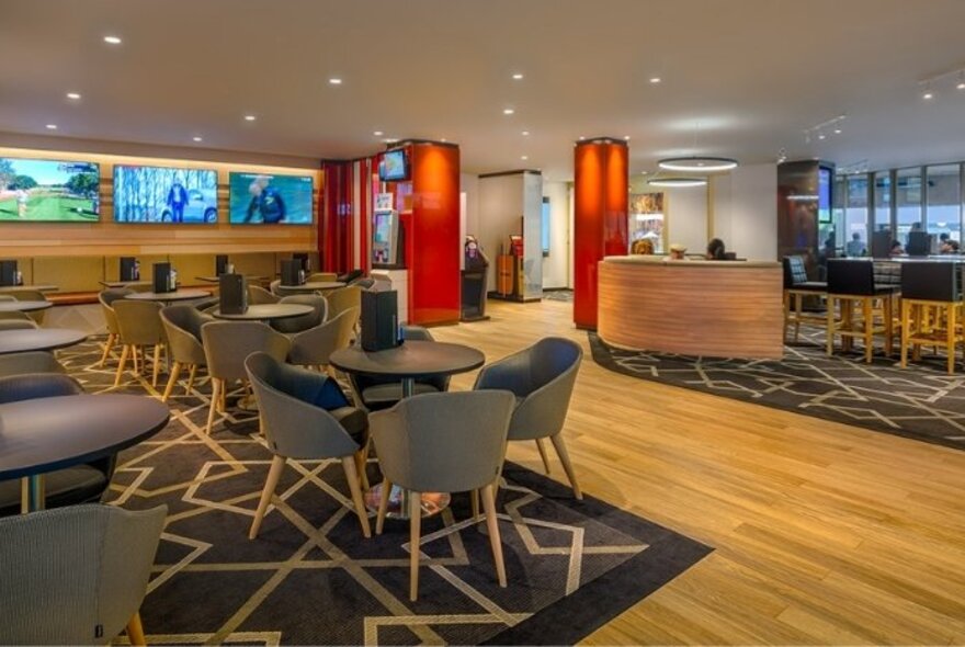 An empty bar interior with curved chairs around round tables and red columns.