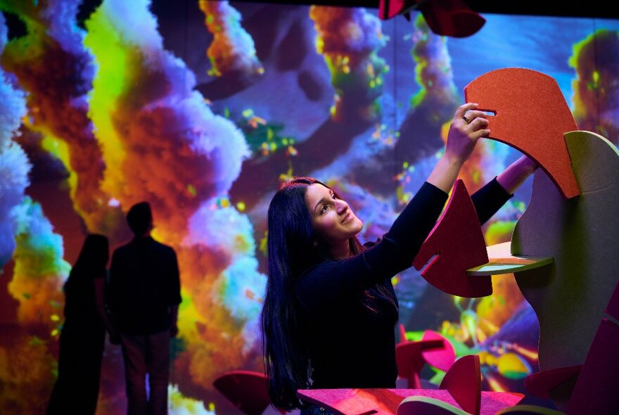 Silhouettes of people in a room with coloured smoke-like effects running down from the ceiling in many colours.