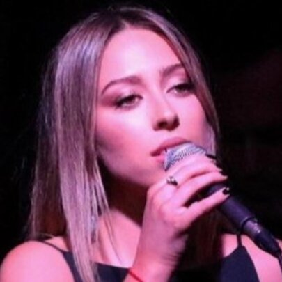 Soulful young singer Jemma Cher singing into a microphone in a pink light.