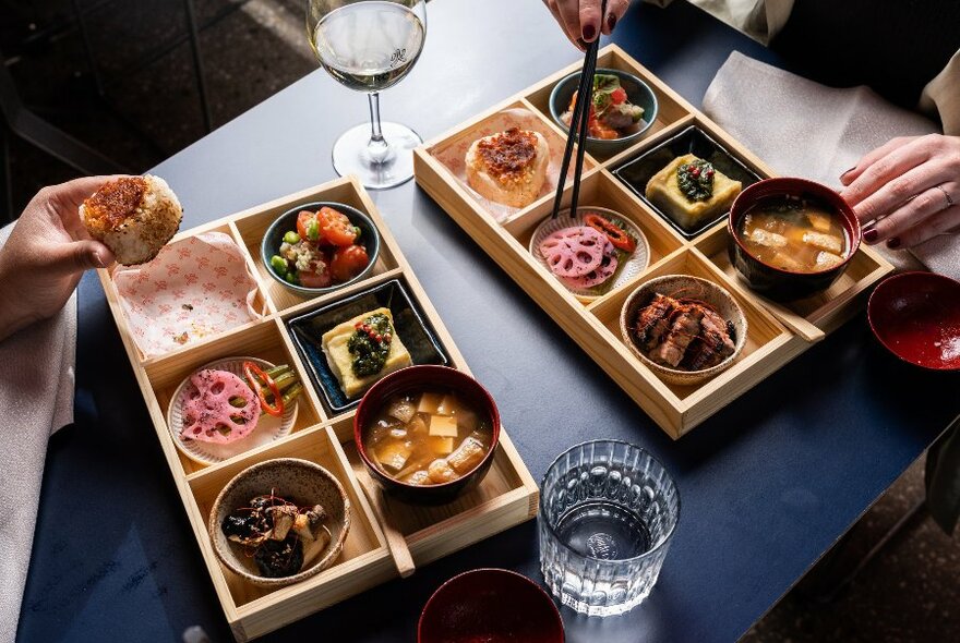 Two people eating bento boxes filled with different dishes.