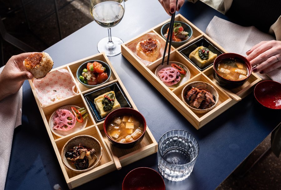 Two people eating bento boxes filled with different dishes.