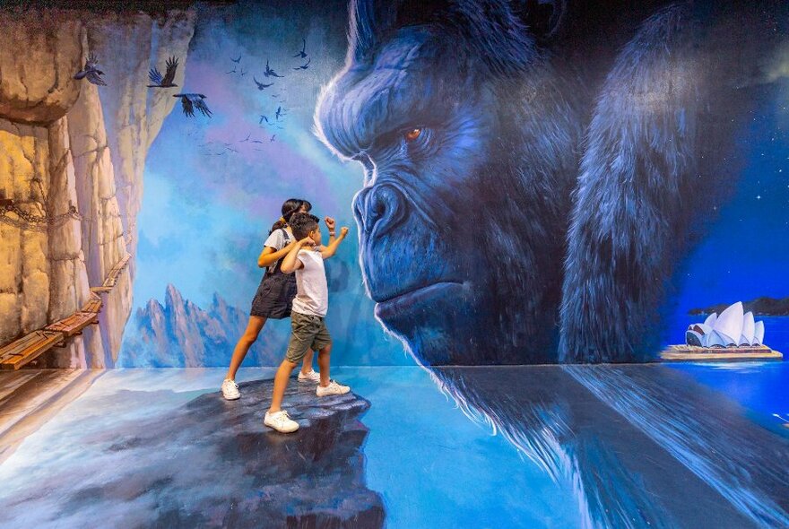 Two children posing in front of a painting of a gorilla.