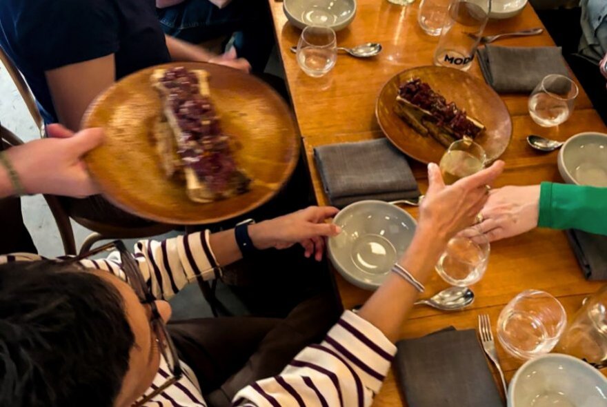 Hands holding glasses and plates of food at a shared cafe table.