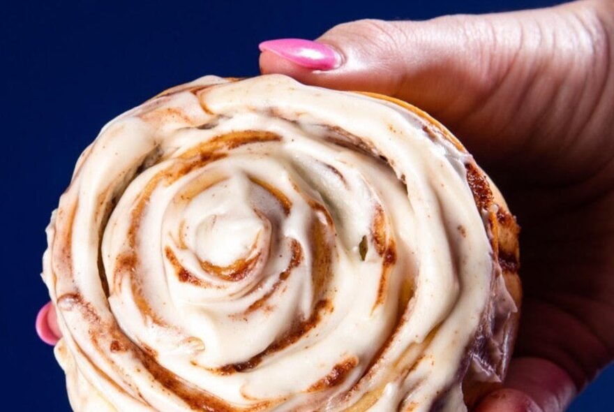 Hand with pink nailpolish holding a cinnamon scroll.