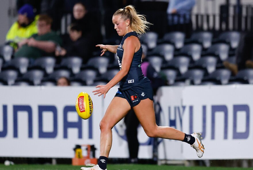 An AFLW player poised to kick a yellow football. 