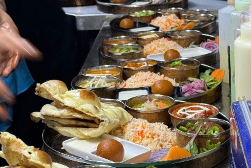 A long line of traditional Indian food presented in small dishes on larger trays.