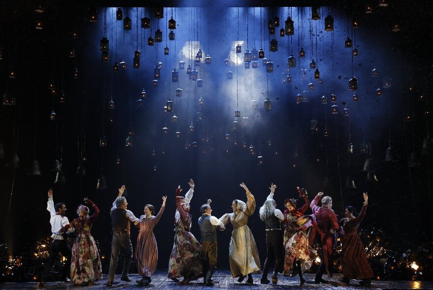 Dancers on stage in Edwardian-era costumes with a foggy night sky set design.