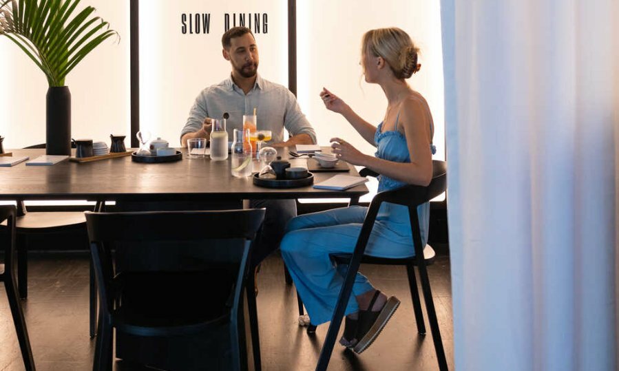 A man and a woman sitting at the end of a black dining table at a minimalist restaurant.