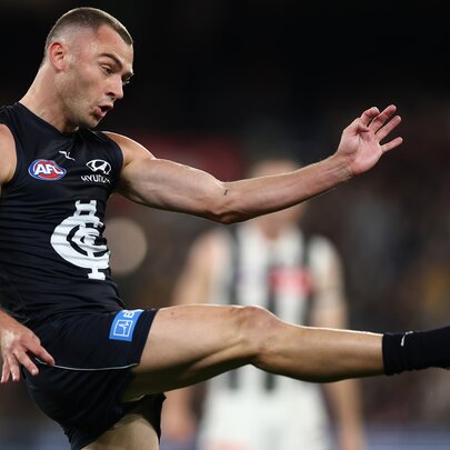 Profile of a Carlton AFL player with his leg raised high in front of him, having just kicked a football.